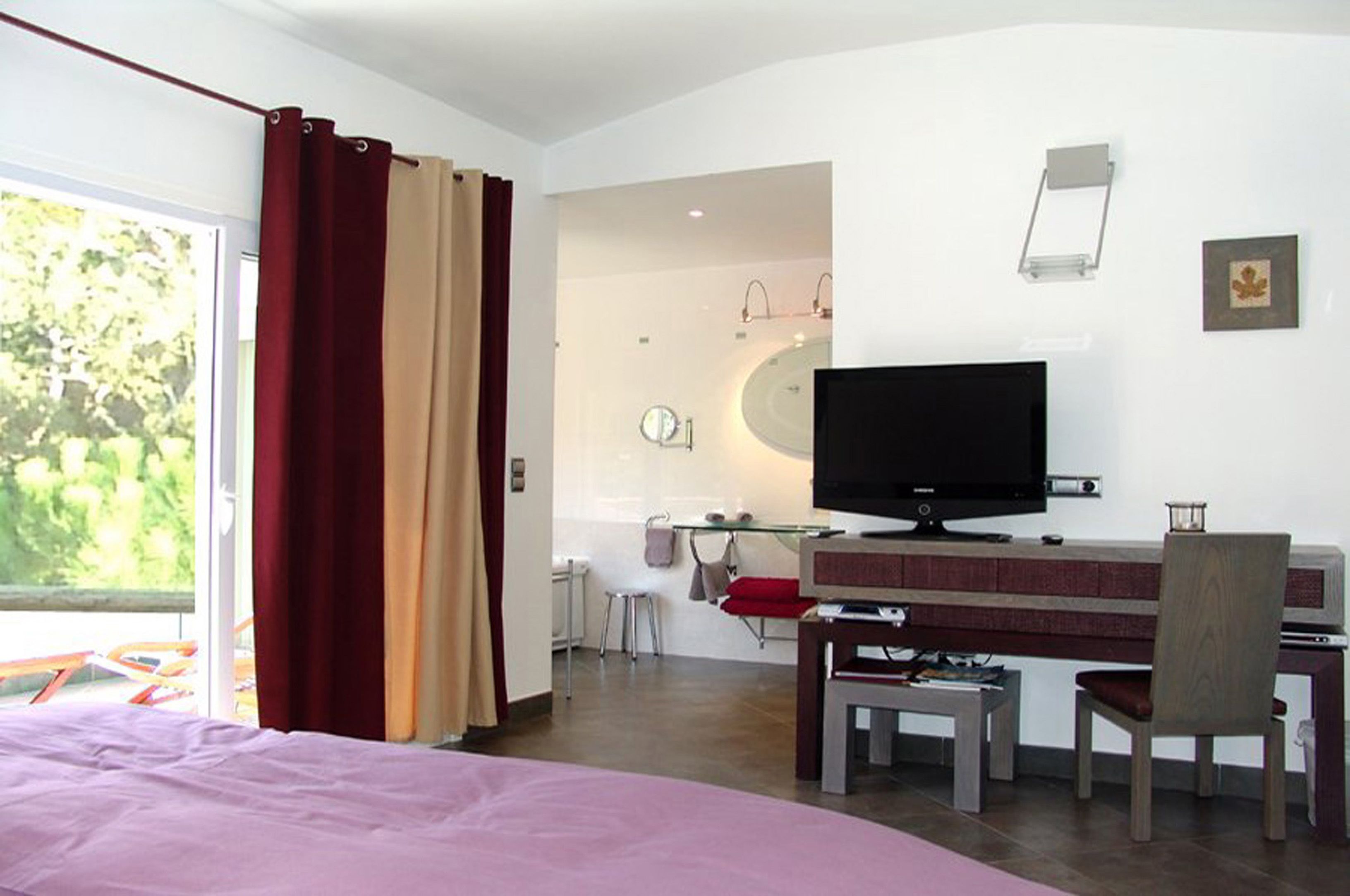 Une chambre d’hôtel avec un lit, un bureau et une chaise, un téléviseur et une salle de bain visible à travers une porte ouverte.