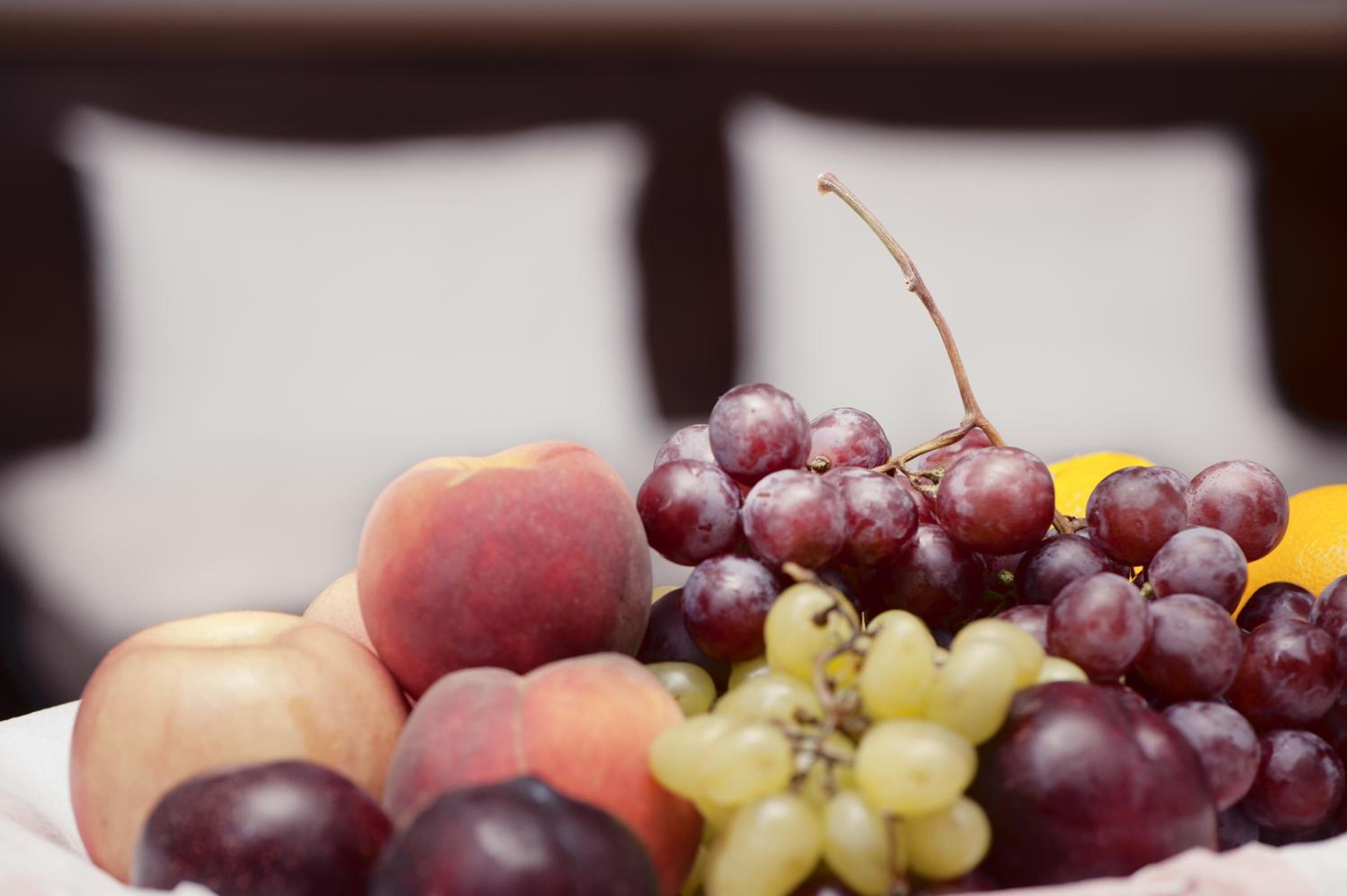 A fruit bowl with peaches, grapes, and an orange.