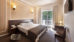 A hotel room with a bed, bedside table, lamp, chair, and a view of the outdoors. - Geneva Resort Hotel (Odesa)