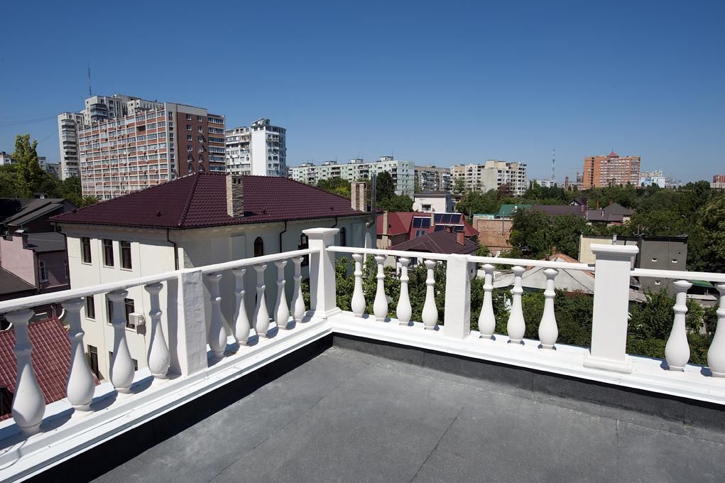 Una terrassa al terrat amb barana blanca, un edifici amb teulada vermella i un paisatge urbà de fons.