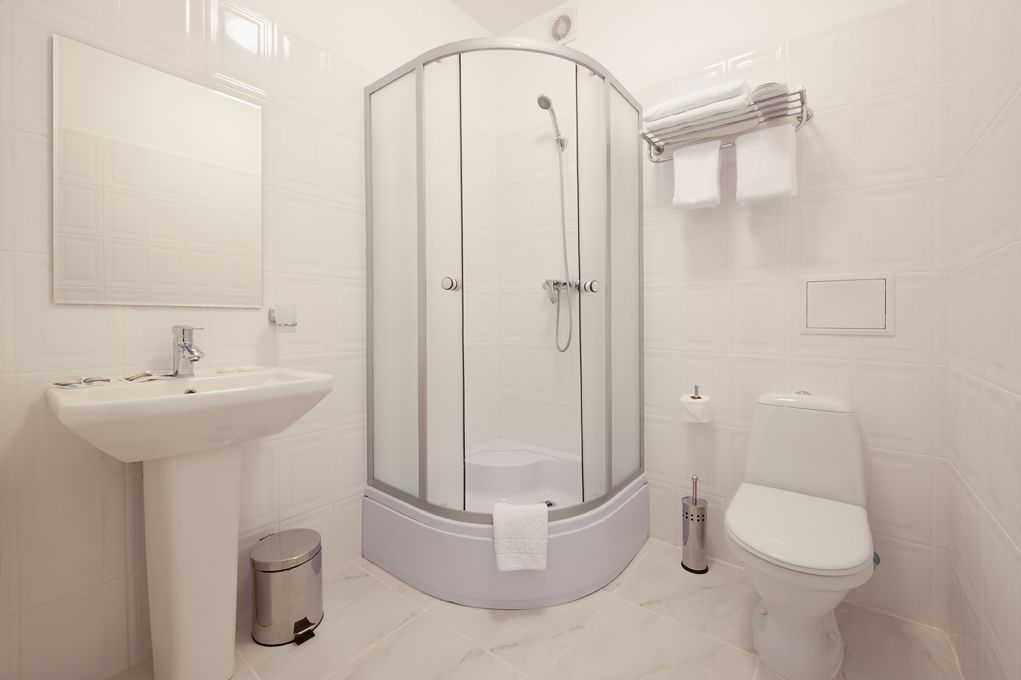 Un baño moderno con ducha envuelta en vidrio, un lavabo pedestal, inodoro y un cubo de basura.