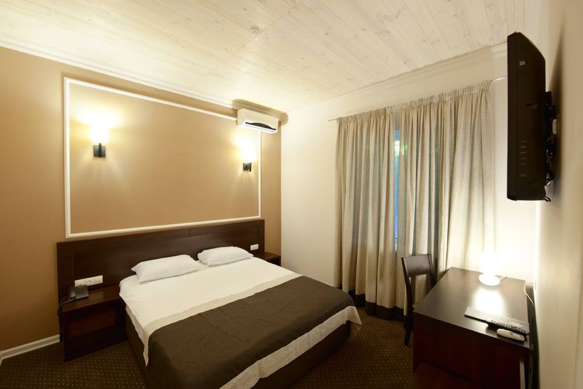 Ein Hotelzimmer mit einem großen Bett, Nachttischen, einem Schreibtisch mit Stuhl, einem wandmontierten Flachbildfernseher und einem Fenster mit Vorhängen.