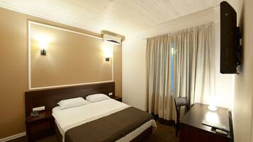 Een hotelkamer met een groot bed, nachtkastjes, een bureau met stoel, een flatscreen-tv aan de muur en een raam met gordijnen.
