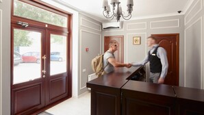 A reception area with a wooden reception desk, a chandelier, and a double door with glass panels. - Geneva Resort Hotel (Odesa)