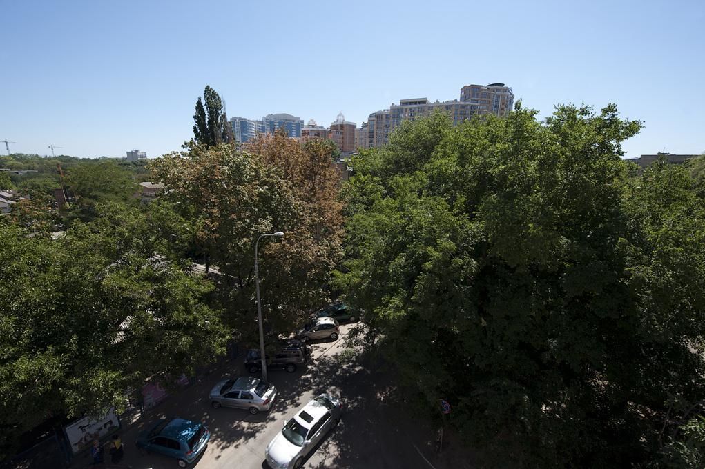 A parking area with several cars, surrounded by trees and buildings in the background.