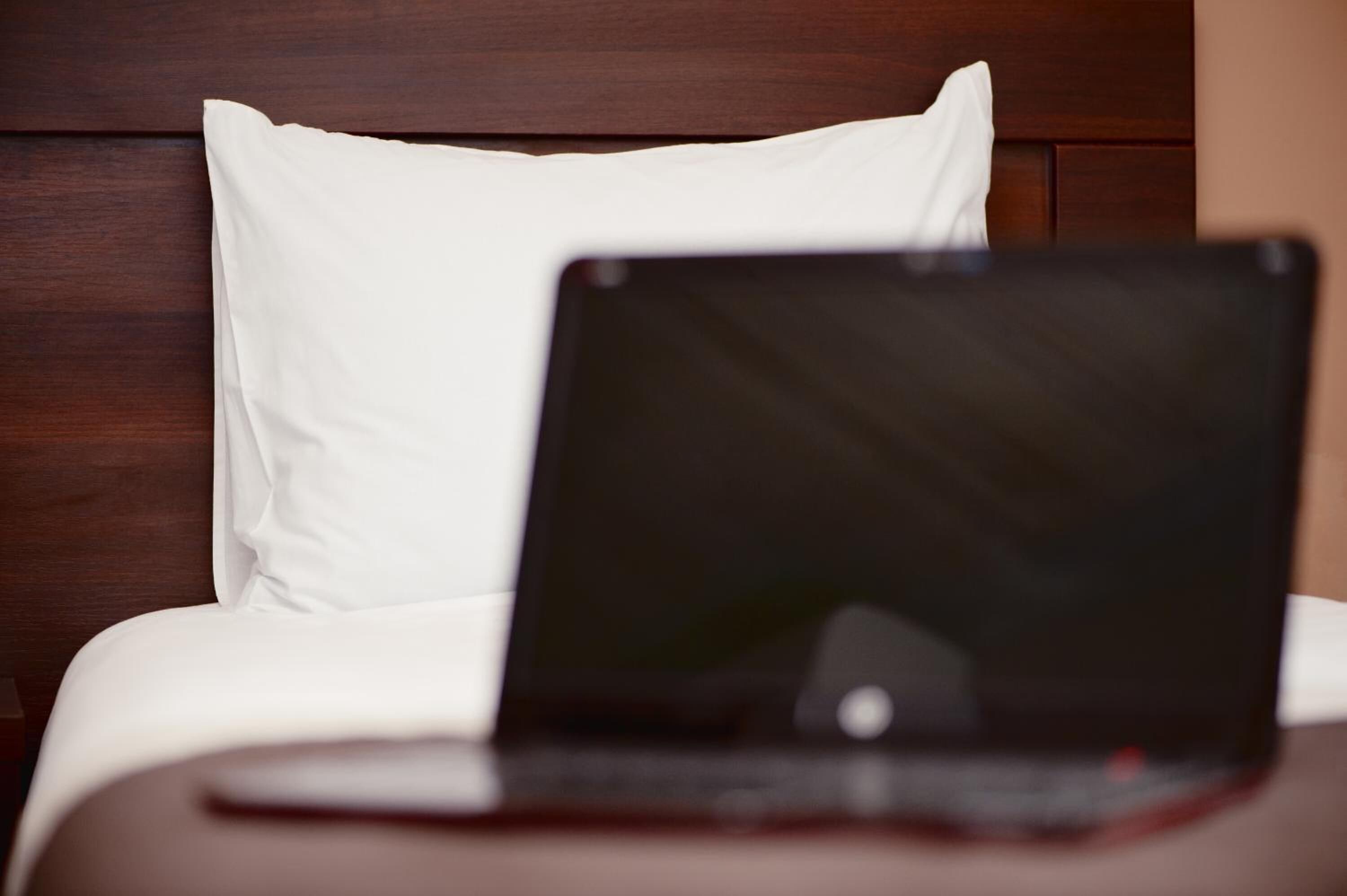 Um laptop sobre a cama, com um travesseiro branco e cabeceira de madeira.