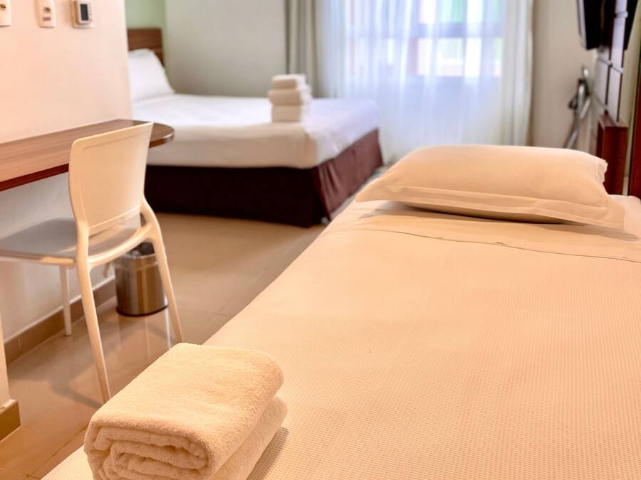 A hotel room with a bed, a chair, a desk, and a window with curtains.