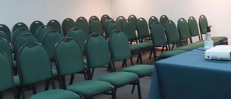 Une salle de conférence avec des rangées de chaises vertes et une table sur laquelle se trouve un projecteur.