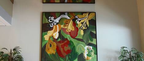 Un hall d’entrée agrémenté de deux tableaux abstraits, d’un banc en bois et de plantes en pot.