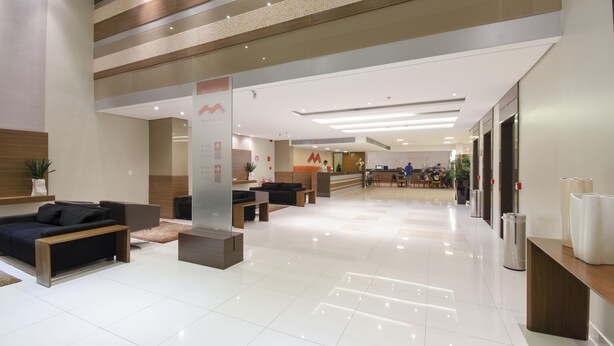Een moderne hotellobby met een receptiebalie, een zithoek en een schone, betegelde vloer.