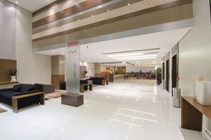 Un moderno vestíbulo de hotel con mostrador de recepción, zona de estar y suelo de baldosas limpias.