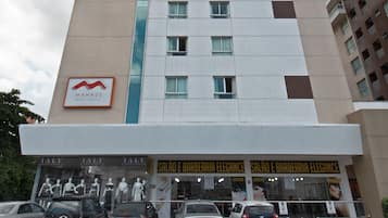A hotel with a prominent 'Hotel' sign, a 'Manaus' logo, and 'Salao e Barberia Elegance' signage. There are several cars parked in front.