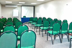 Un salón de conferencias con filas de sillas verdes, una pizarra y una pantalla para proyector.