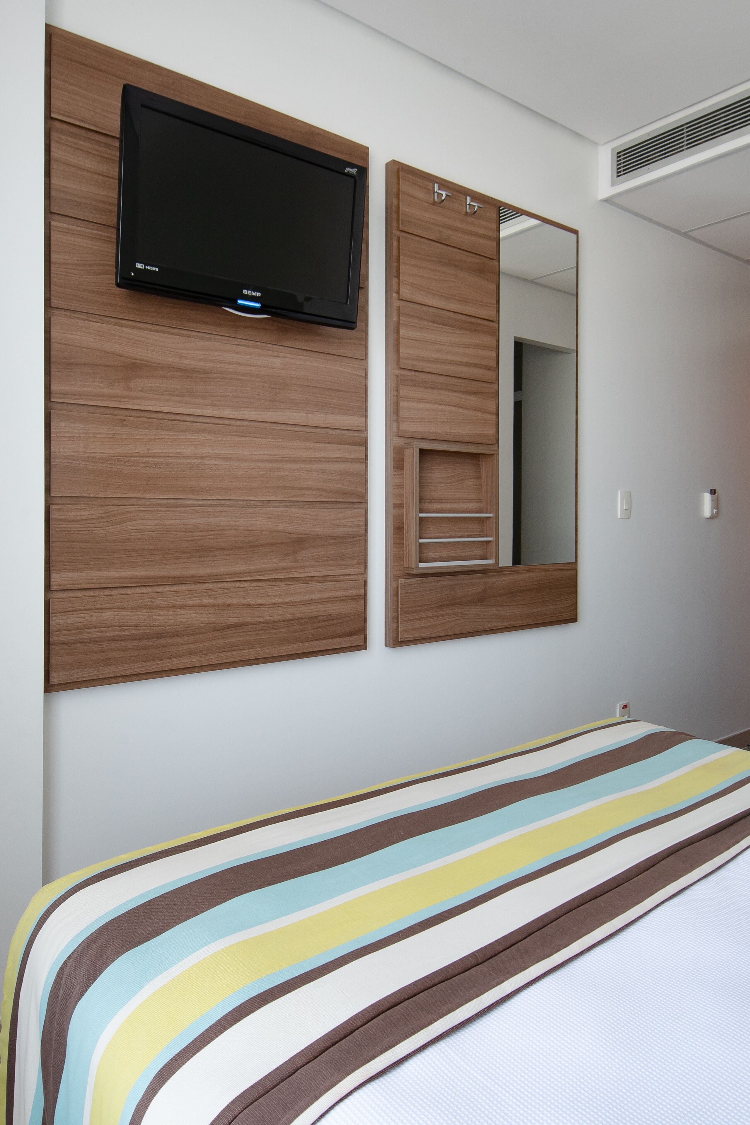 A hotel room with a bed, a television mounted on a wooden panel, and a mirror.