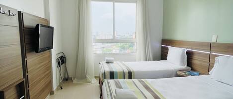 A hotel room with two beds, a TV, a window with a city view, and a ceiling light.