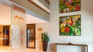 Een receptiehal met een glazen wand, een receptiebalie, een bank en twee bloemstillevens.