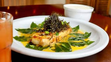 Prato com peixe grelhado, vegetais e uma pequena tigela de arroz ao fundo.
