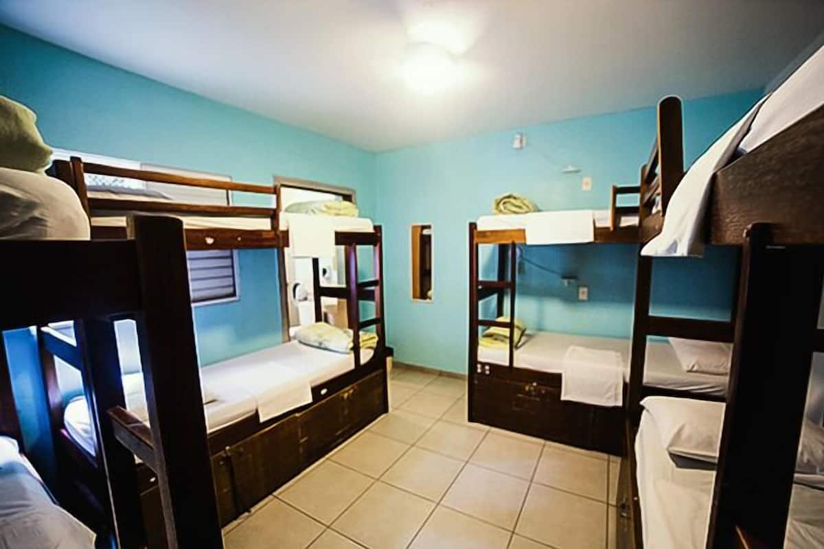 Ein Schlafsaalzimmer mit Etagenbetten, einem kleinen Fenster und einer Deckenleuchte.