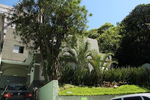 Stucco and stone building with a flat roof, set amidst a lush garden with palm trees and shrubs.