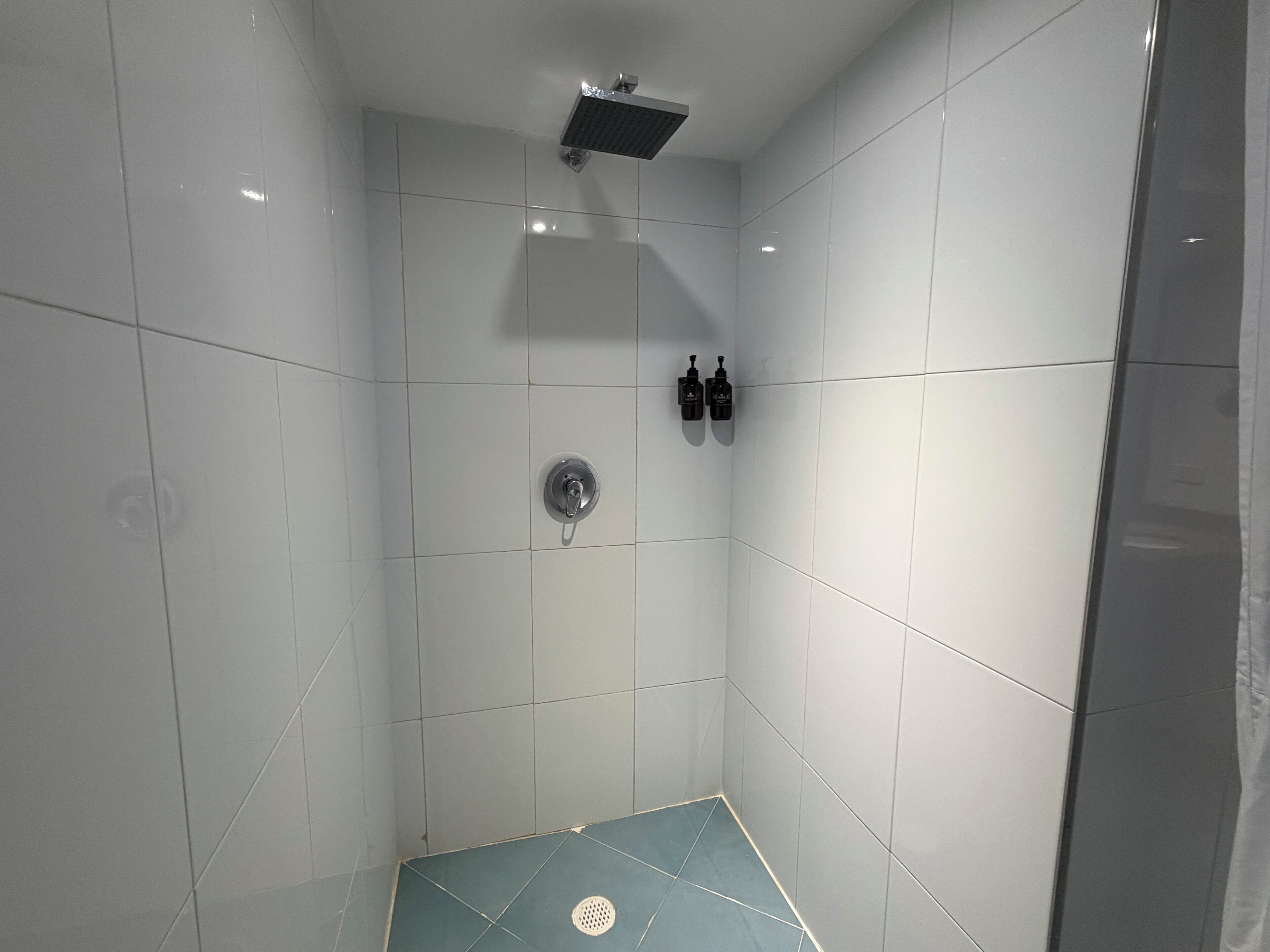 A shower with white tiles, a showerhead, and two bottles of shampoo.