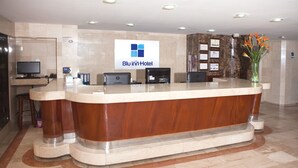 A hotel reception desk with a logo, a computer, and a vase with flowers. - Blu Inn Hotel (Bogotá)