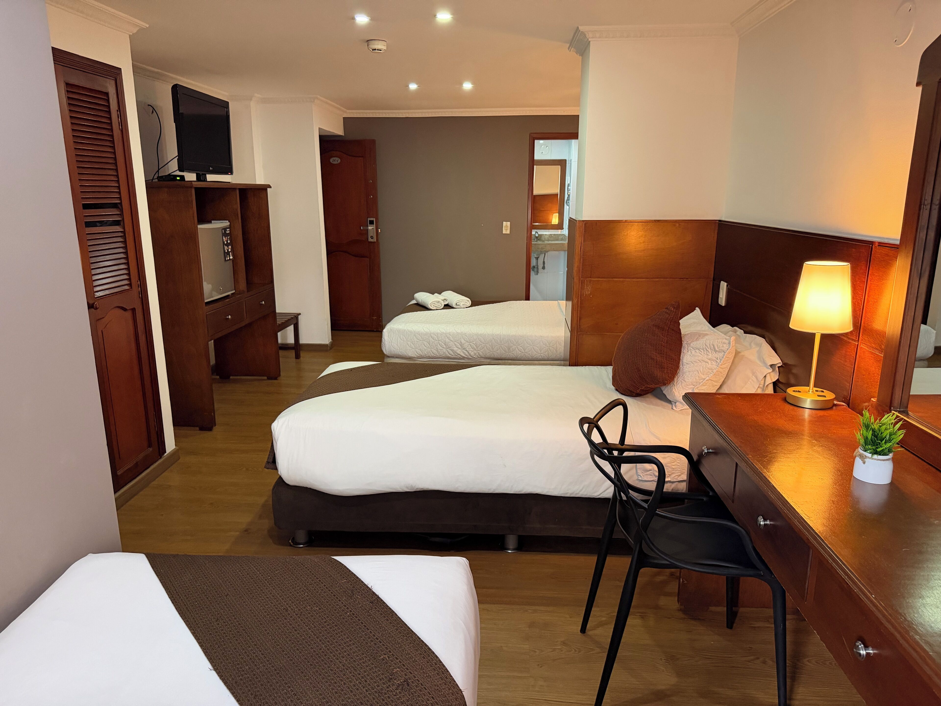 A hotel room with two beds, a desk, a chair, a lamp, and a television.