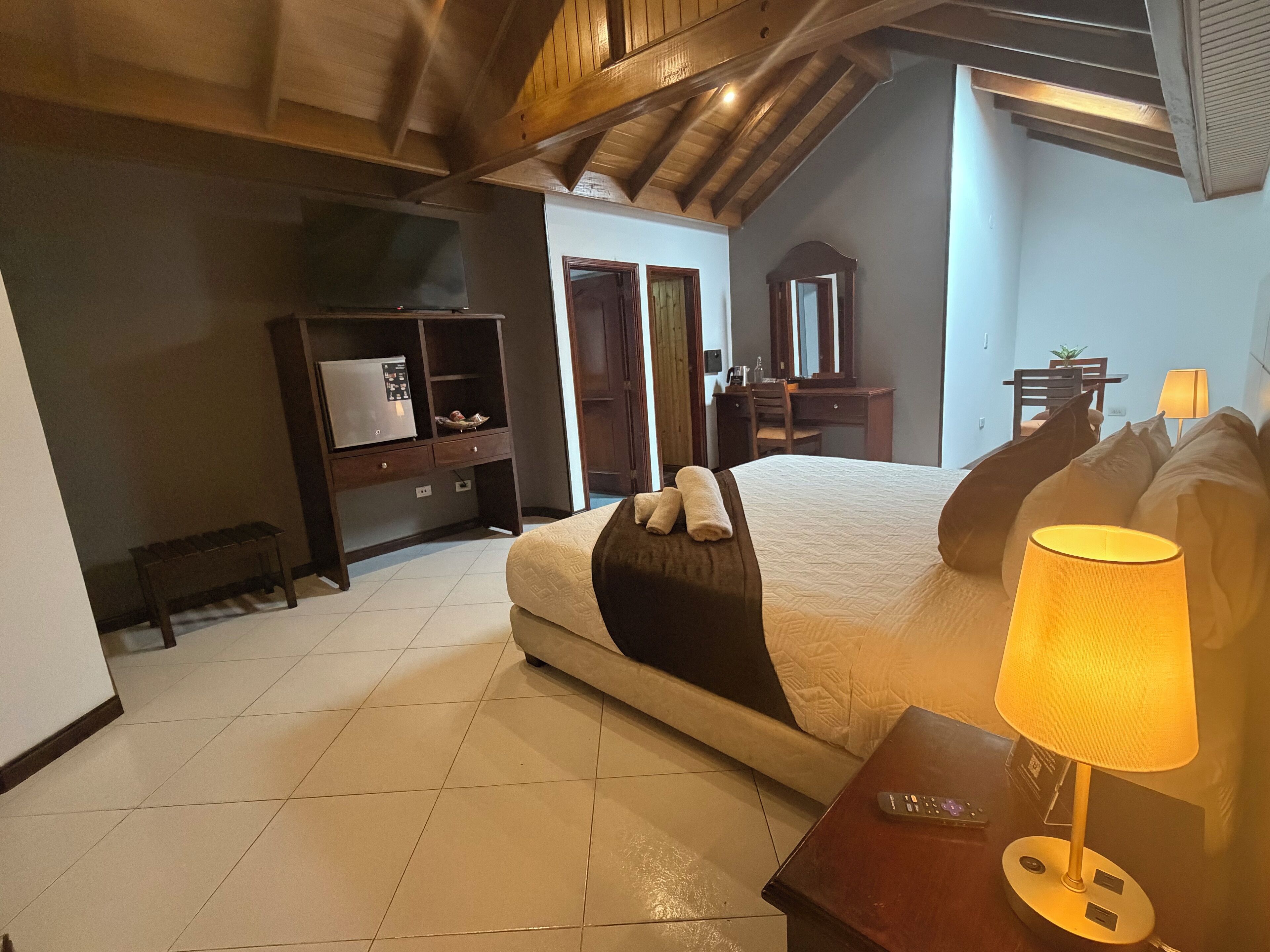 A bedroom with a bed, a bedside table with a lamp, a dresser, a mirror, and a television.