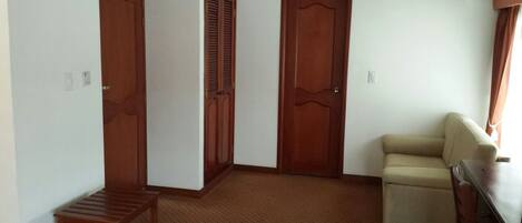 Une pièce avec trois portes en bois, un canapé beige, un banc en bois et une petite table.
