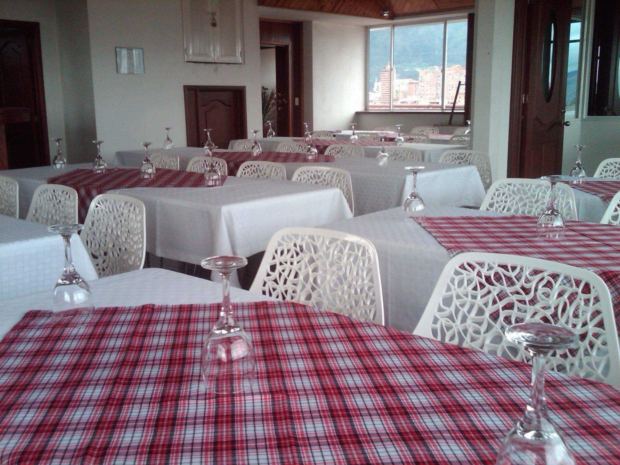 Un comedor con mesas dispuestas para el servicio, sillas blancas y vistas a edificios a través de las ventanas.