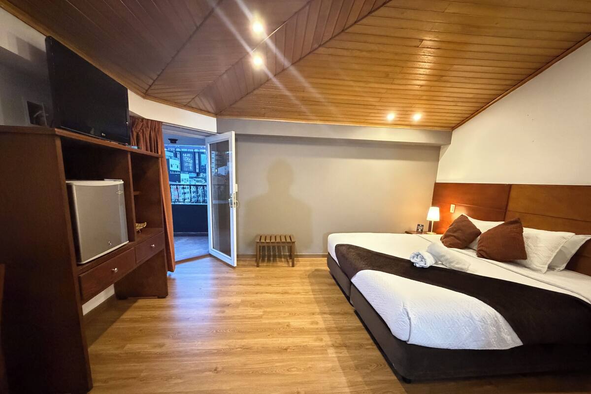 A hotel room with a bed, bedside table, lamp, and a television on a shelf.