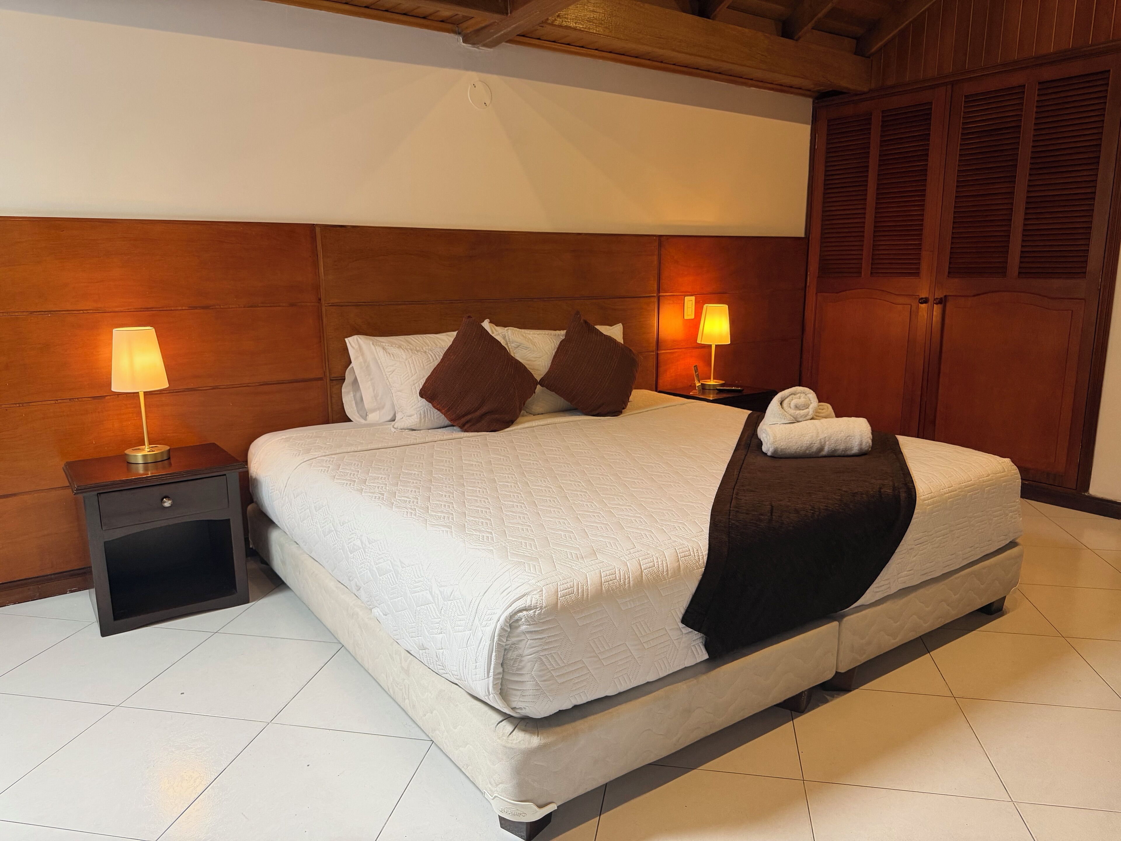 A neatly made bed with pillows, a bedside lamp, and a rolled towel on the bed.