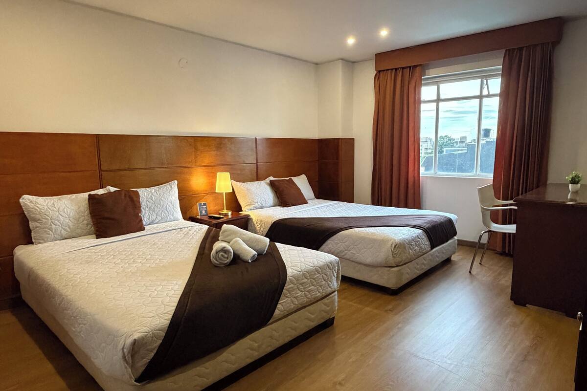 A hotel room with two beds, a desk, a chair, and a window with curtains.