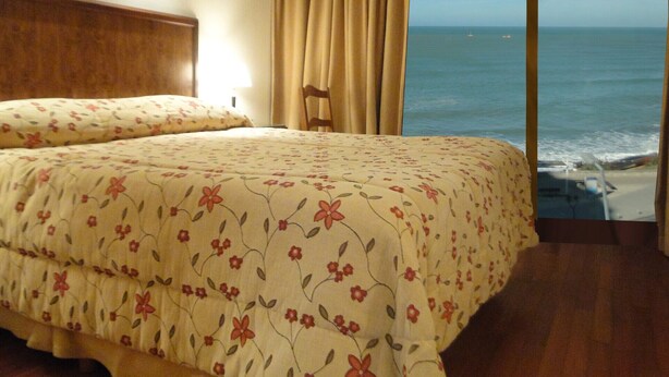 A bedroom with a bed, a wooden headboard, a view of the ocean, and a curtain. - Hotel Amsterdam (Mar Del Plata)