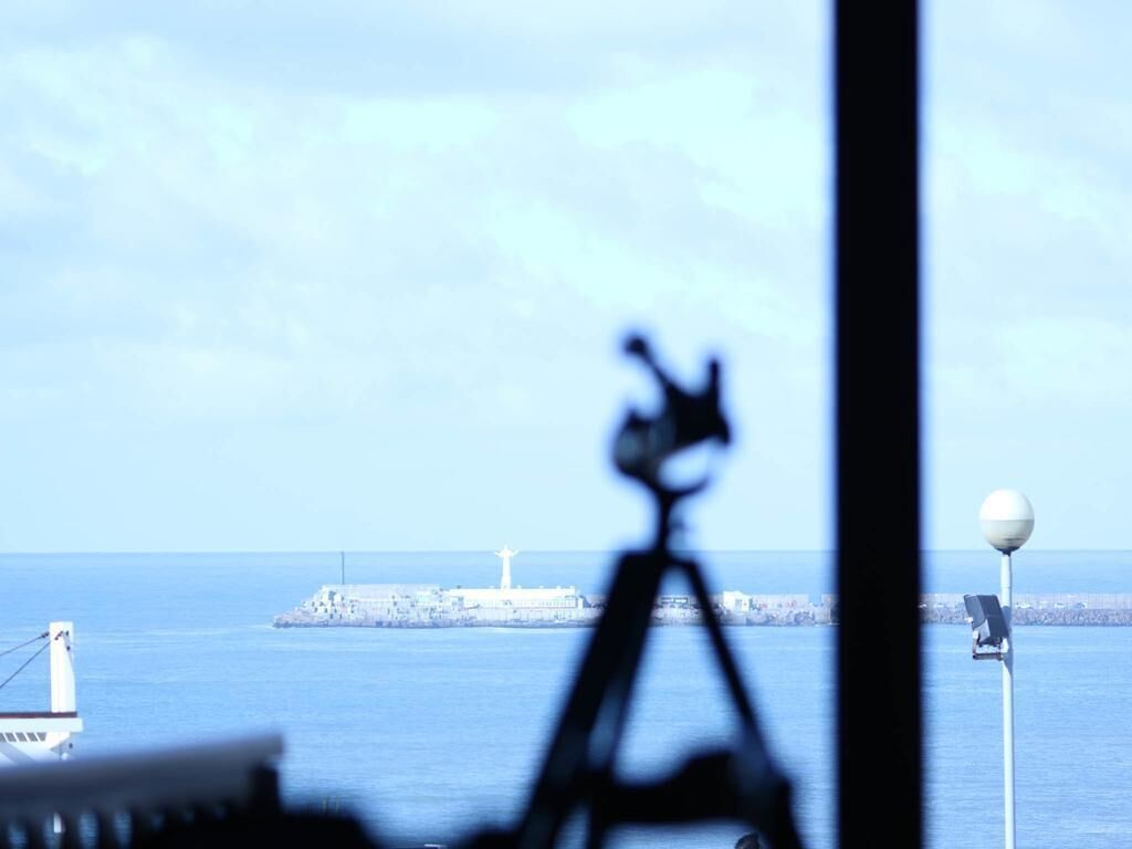 A view of a lighthouse and a pier with a tripod in the foreground.