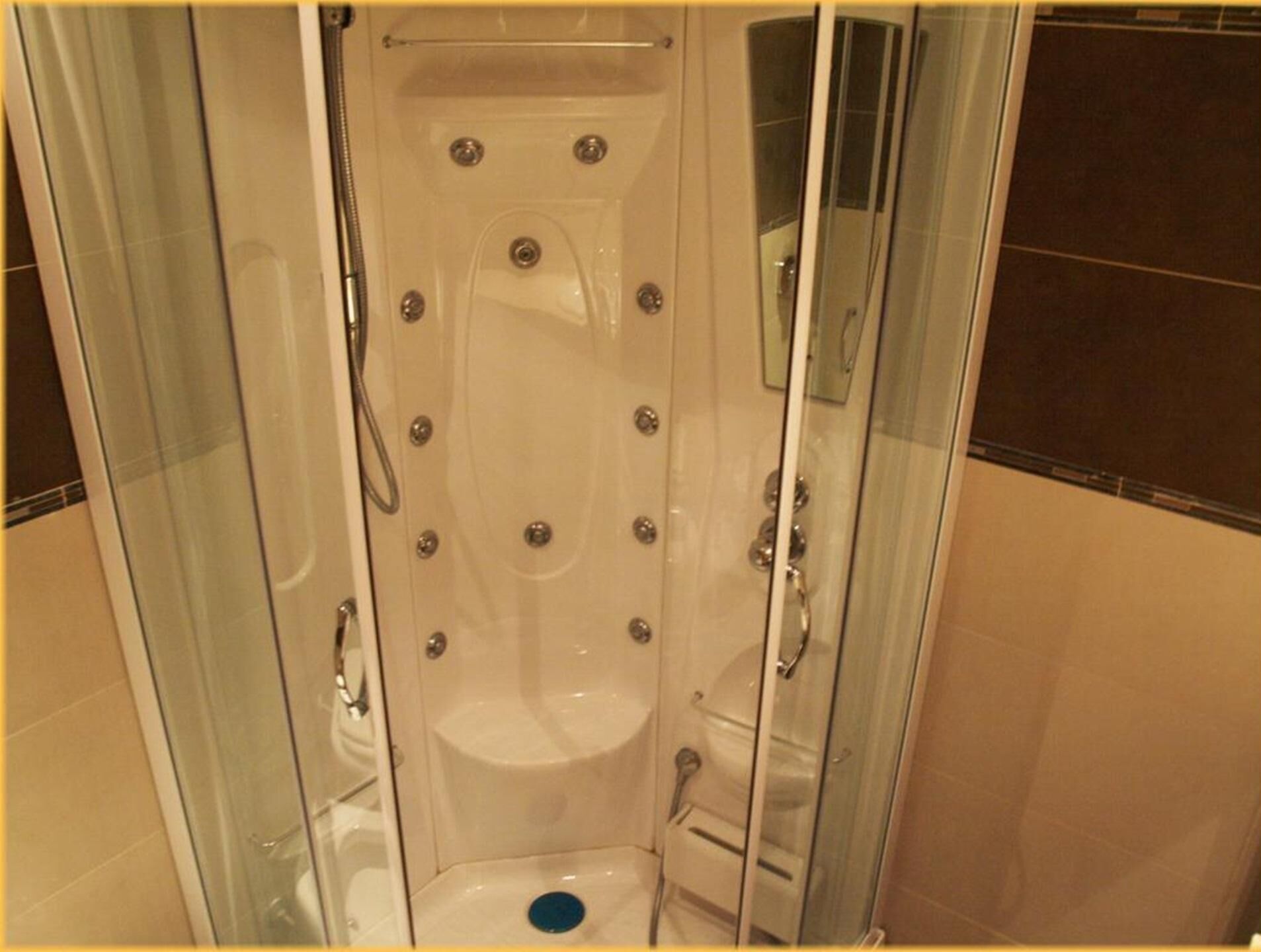 Cabina de ducha con paredes de vidrio, múltiples grifos y un asiento integrado.