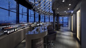 Un bar moderno con vistas panorámicas de la ciudad, techo alto con luces colgantes y una amplia selección de vinos.
