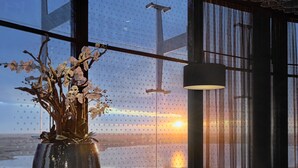 Un interior moderno con un jarrón grande de orquídeas, dos sillones, una mesita y vistas a la puesta de sol a través de una ventana con diseño.