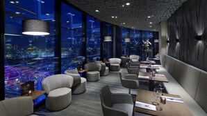 Un restaurante moderno con vistas a la ciudad, con asientos redondos, iluminación colgante y una pared texturizada oscura.