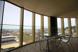 A balcony with large windows, a table, and chairs.