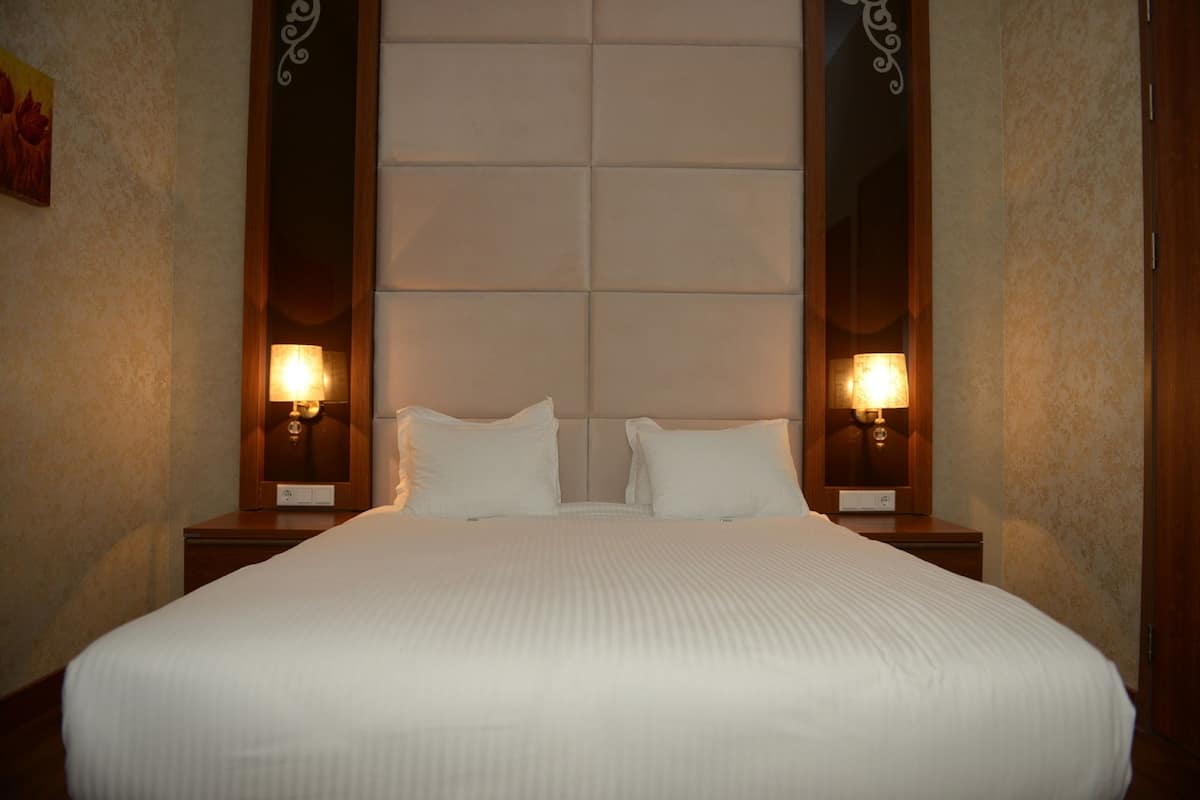 A hotel room with a large bed, two bedside tables with lamps, and a headboard with a mirror.