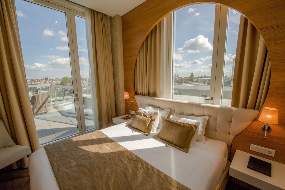 A hotel room with a large bed, a view of the city, and a wooden ceiling.