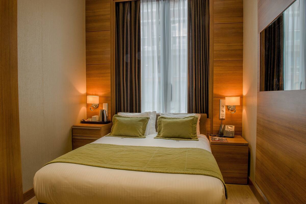 A hotel room with a bed, two bedside tables, a lamp on each table, and a window with curtains.