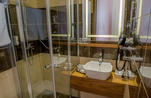 Moderni kylpyhuone, jossa on lasiseinällä varustettu suihku, valkoinen pesuallas ja puinen allaskaappi.