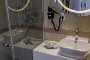 A bathroom with a glass-enclosed shower, a white sink, and a hairdryer mounted on the wall.