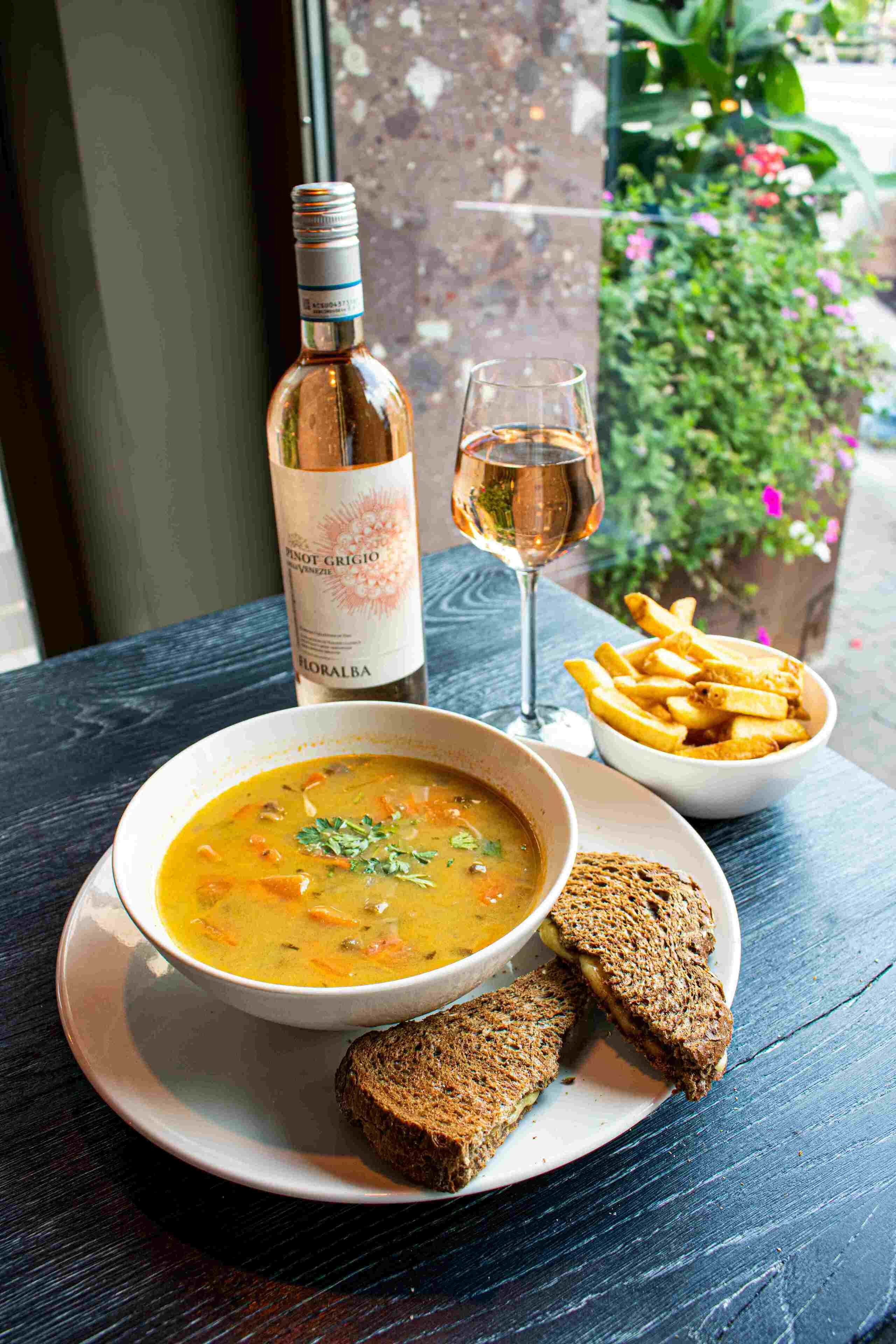 A bowl of soup with bread and fries on a table with a bottle and glass of wine.
