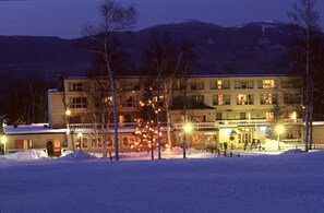 Un albergo con diversi piani, terreno innevato e una montagna sullo sfondo.