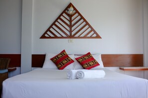 Quarto de hotel com uma cama, duas almofadas vermelhas com desenhos de elefantes, uma cabeceira de madeira e um candeeiro fixado na parede.