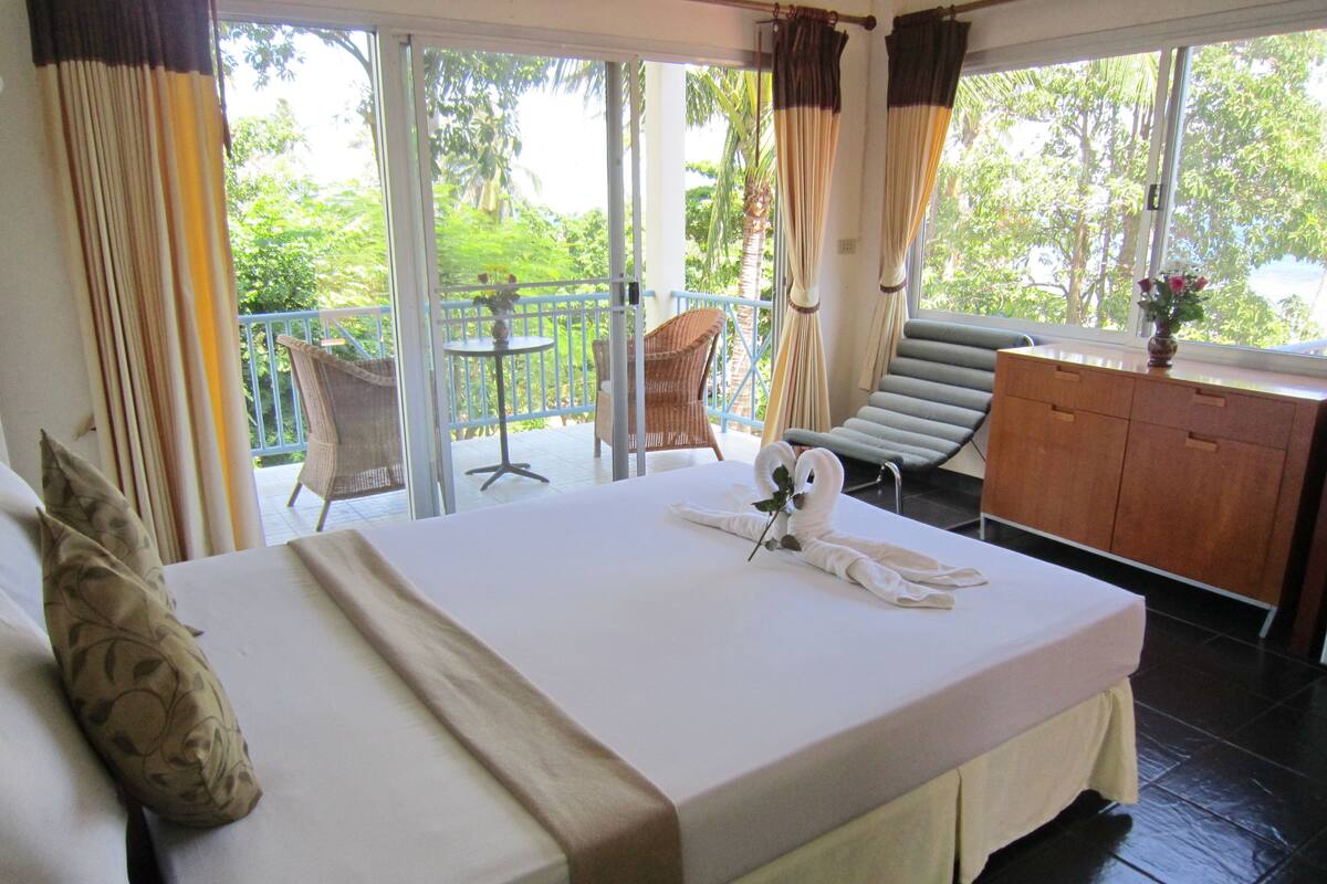 A hotel room with a bed, a small table, a chair, and a view of the outdoors.