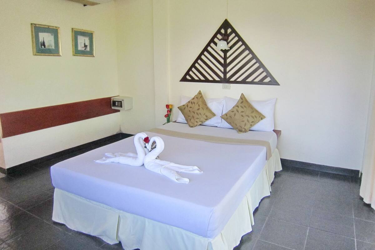 A hotel room with a bed, a bedside table with a vase of flowers, and a wall-mounted air conditioner.