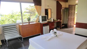 A hotel room with a bed, a desk, a television, a small refrigerator, and a window with curtains. - Thaniza Beachfront Resort (Ko Pha-ngan)